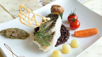 A white plate with a variety of food items including a piece of grilled fish, cherry tomatoes, a carrot, and some pickled vegetables.