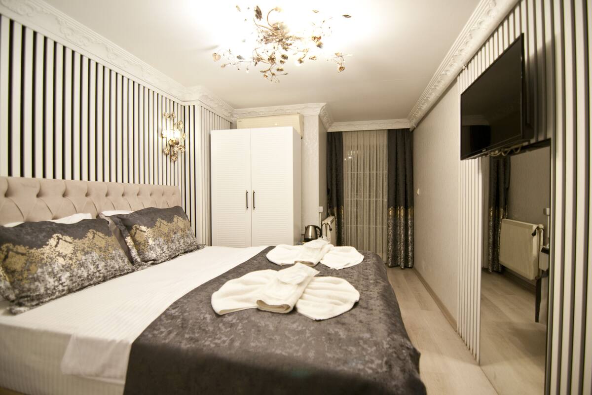 A bedroom with a large bed, a wardrobe, a television, and a chandelier.