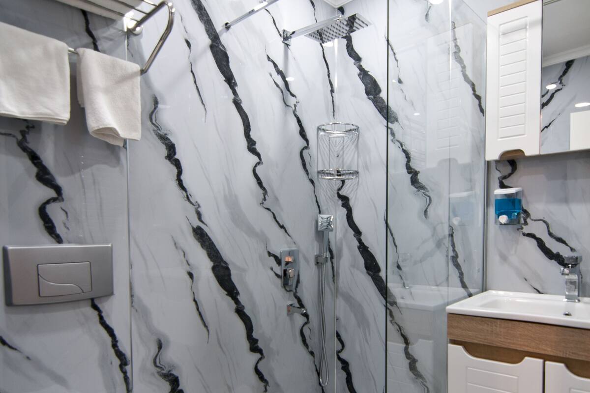 A modern bathroom with a glass-enclosed shower, marble walls, a white sink, and a toilet.