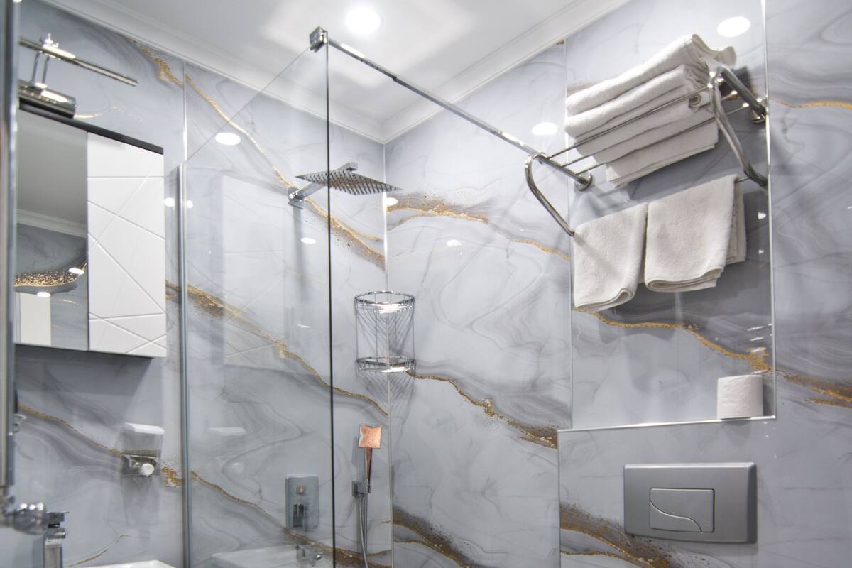 A modern bathroom with a glass-enclosed shower, a white sink, and a marble-tiled wall.