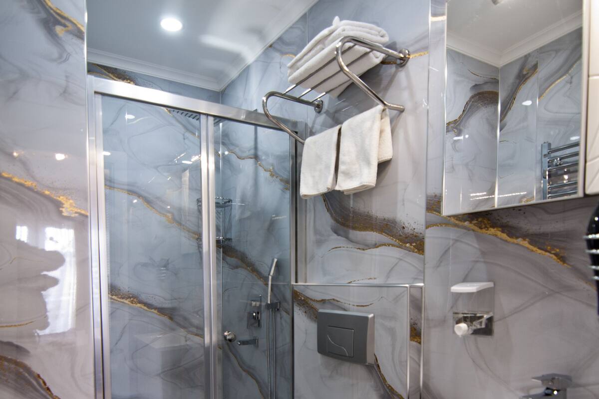 A modern bathroom with a glass-enclosed shower, a white sink, and marble walls.