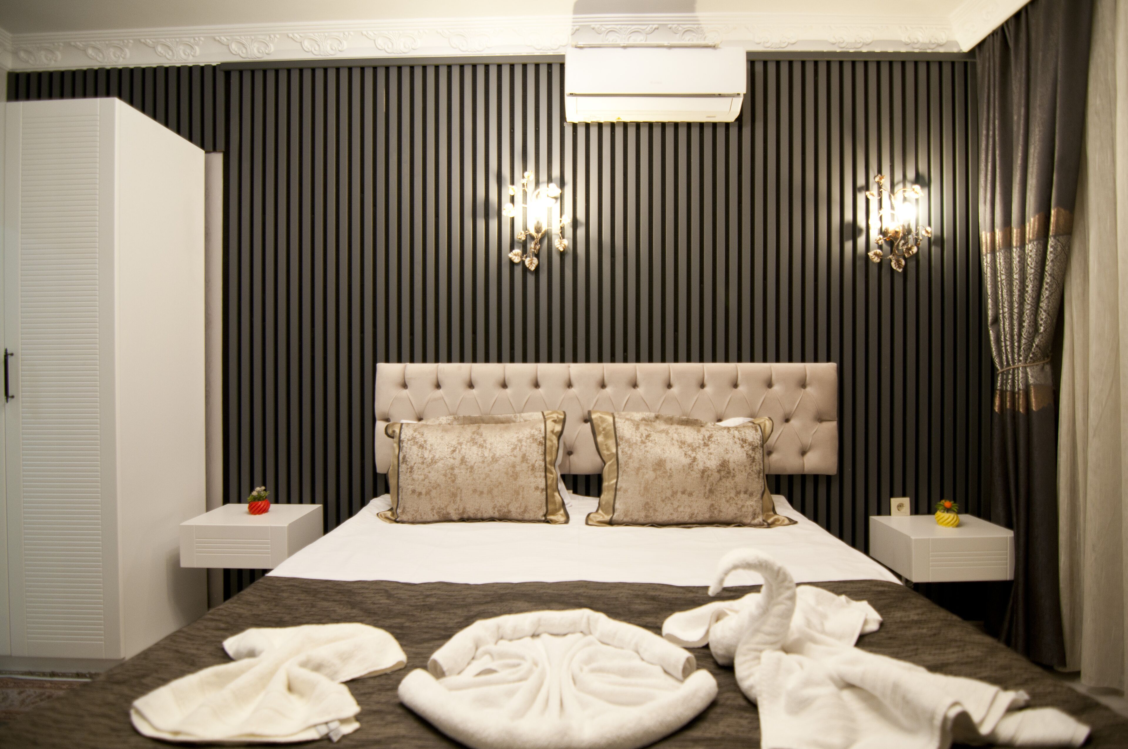 A hotel room with a large bed, two bedside tables, a wardrobe, and a wall-mounted air conditioner.