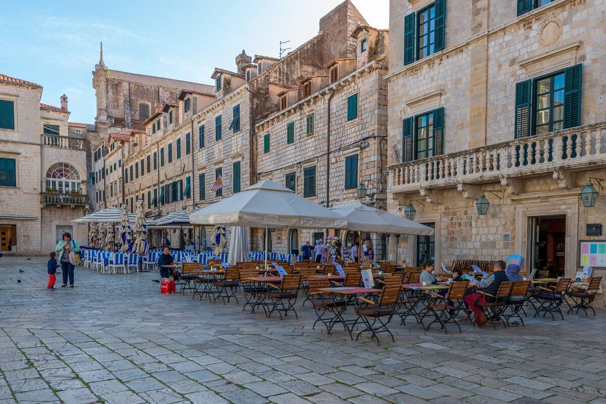 A cobblestone square with outdoor seating, stone buildings, and a fountain.