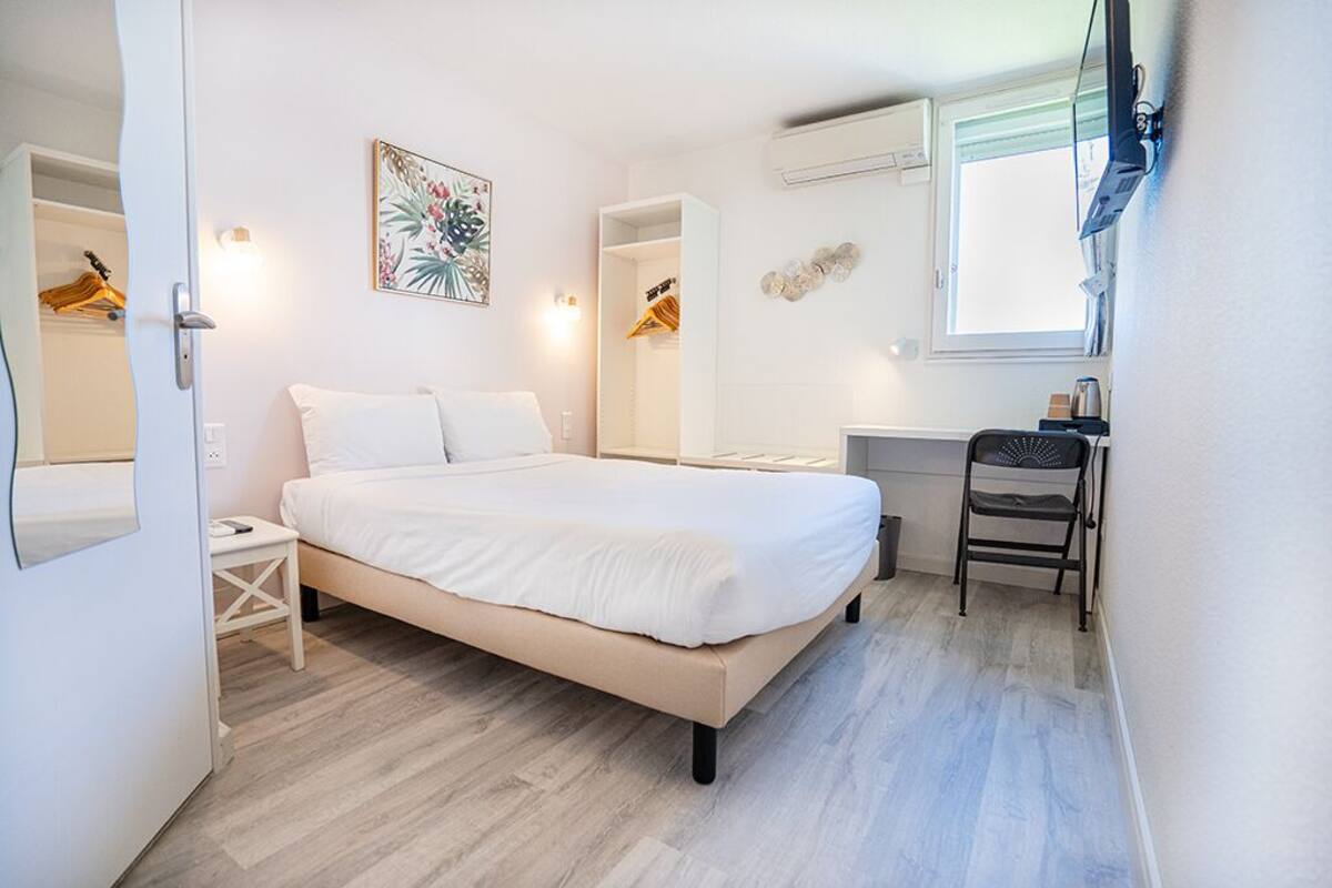 Un dormitorio con cama, mesita de noche, silla, escritorio y ventana.