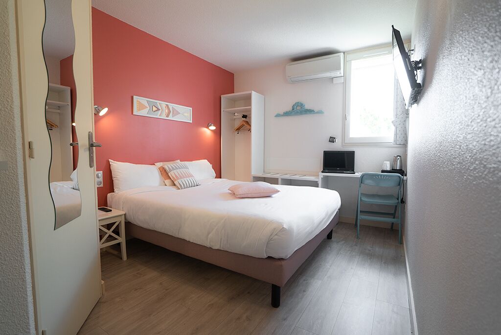 A bedroom with a bed, bedside tables, a desk, and a chair. There is a window with an air conditioning unit above it.