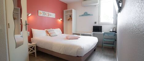 A bedroom with a bed, bedside tables, a desk, and a chair. There is a window with an air conditioning unit above it.