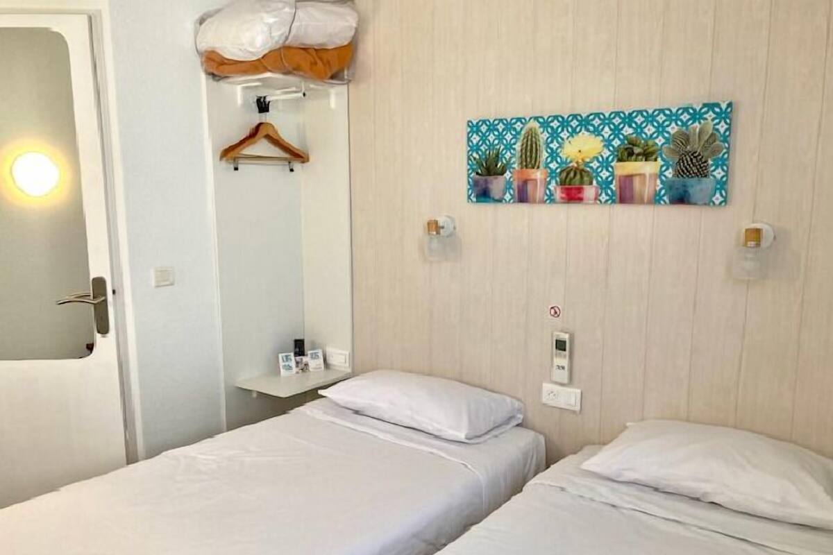 Habitación de hotel con dos camas, cabecera de madera, obra de arte en la pared con cactus y un estante pequeño con artículos de tocador.