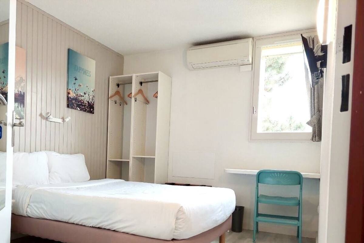 Un dormitorio con cama, escritorio, silla, armario y aire acondicionado.