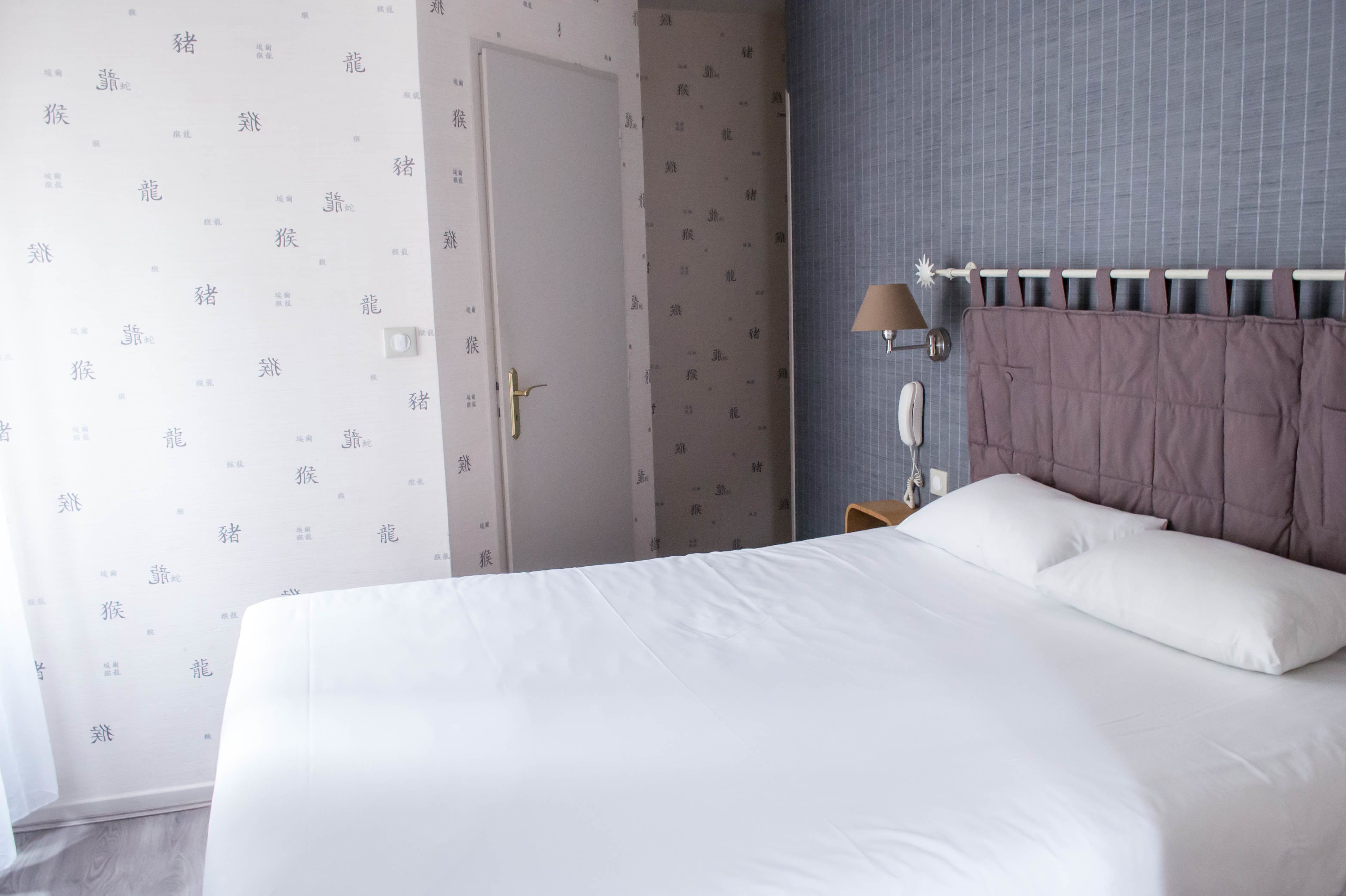 A hotel room with a large bed, a bedside table with a lamp, and a door.