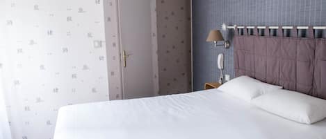 A hotel room with a large bed, a bedside table with a lamp, and a door.