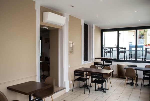 A modern dining area with multiple tables and chairs, a large window with a view, and an air conditioning unit on the wall.