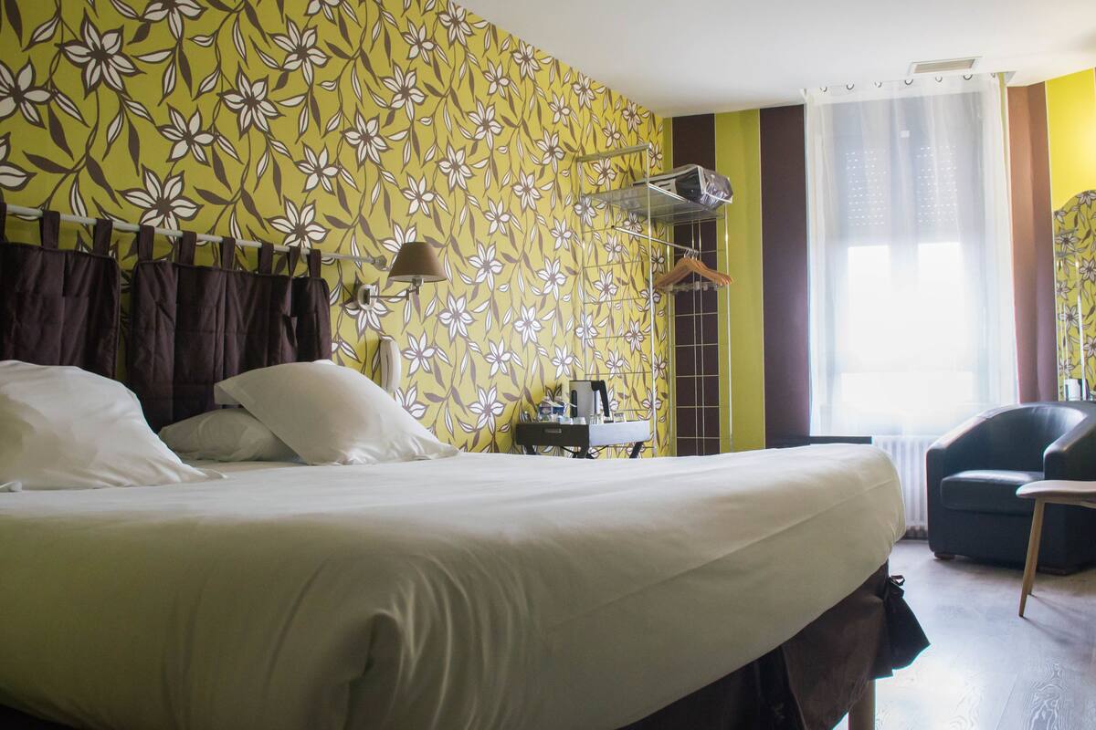 A hotel room with a bed, a chair, a table, and a window with curtains.