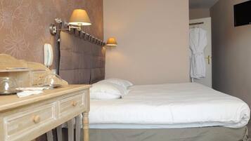 A hotel room with a bed, bedside lamps, a desk with a telephone, and a robe hanging on the door.