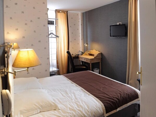 A hotel room with a bed, a desk, a chair, a television, and a lamp.