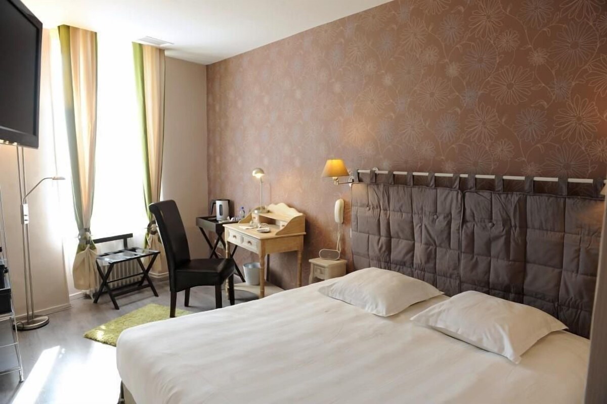 A hotel room with a bed, a desk, a chair, a telephone, and a television.
