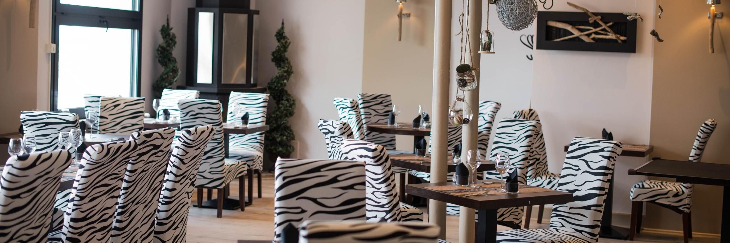 Un restaurant avec des chaises et des tables à rayures zébrées, une grande fenêtre et des œuvres d’art décoratives sur les murs.