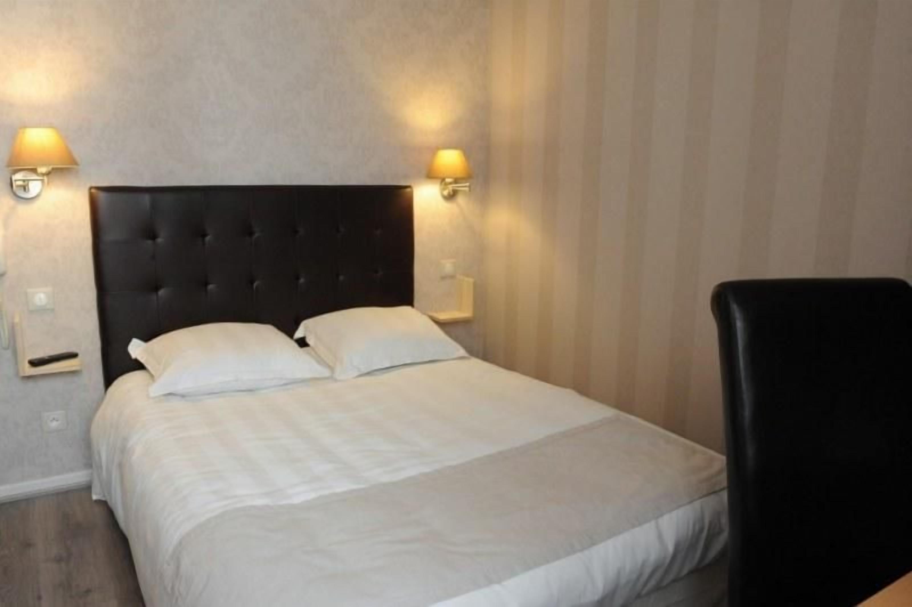 Una cama bien tendida con sábanas blancas y un cabecero negro, con dos lámparas fijadas a la pared a cada lado.