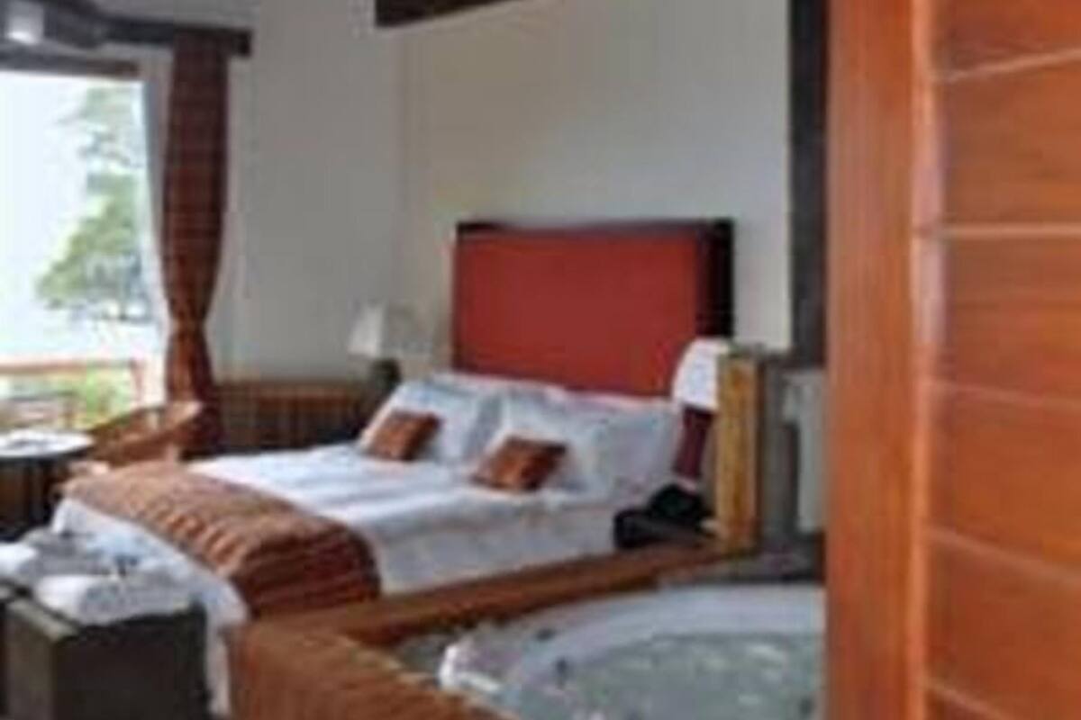 A hotel room with a wooden ceiling, a large bed with red headboard, a small table, and a view of the outdoors.