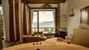 A spa room with a large bathtub, a stone wall, a wooden ceiling, and a view of the sea. - La Sirenuse Lake Resort (San Carlos de Bariloche)