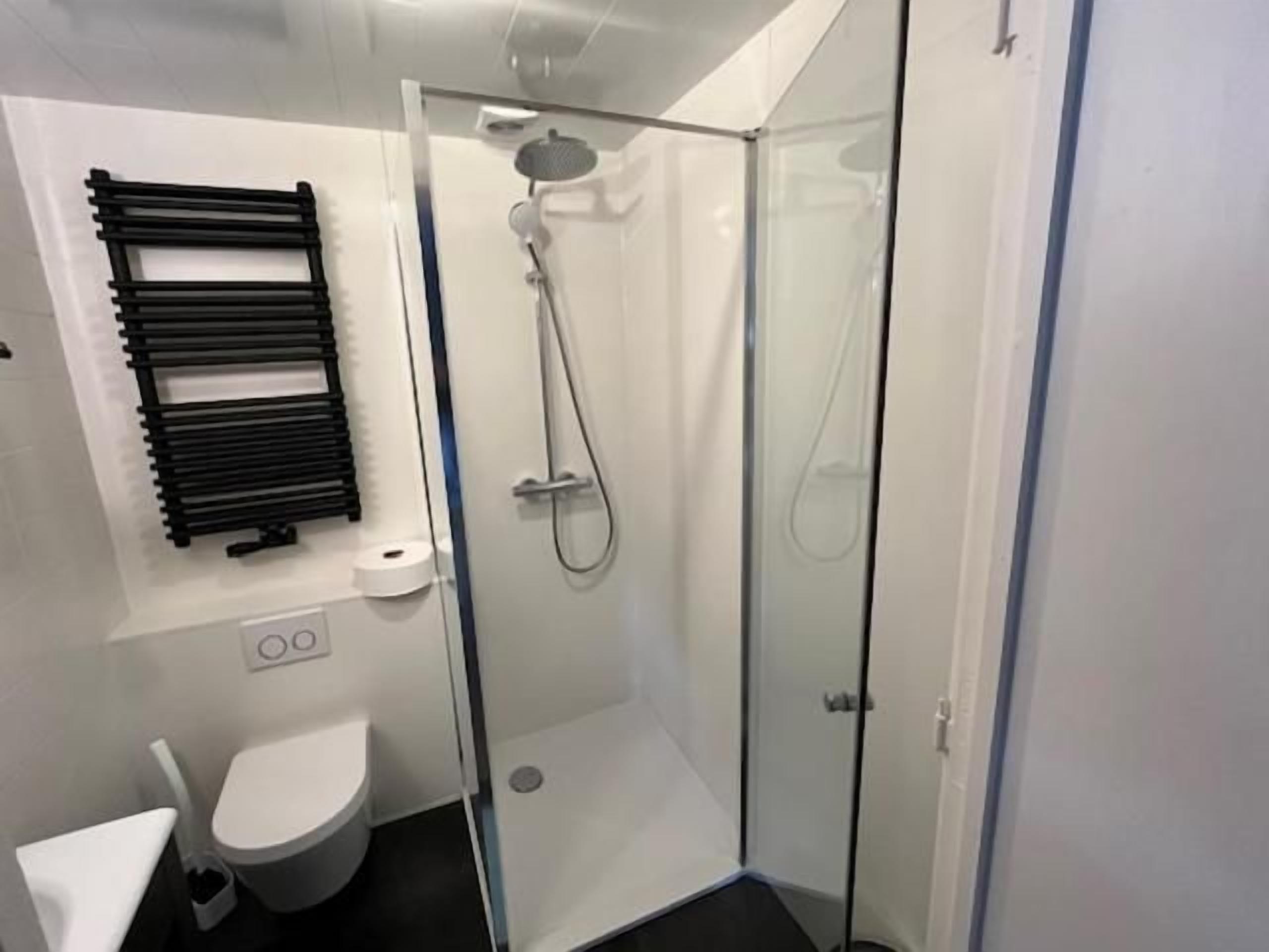 A modern bathroom with a glass shower enclosure, a toilet, and a towel rack.