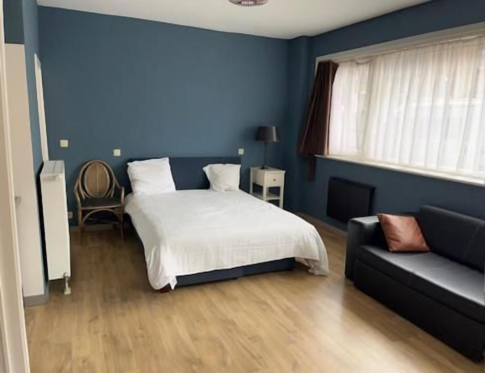 A bedroom with a bed, bedside table, lamp, and a sofa.