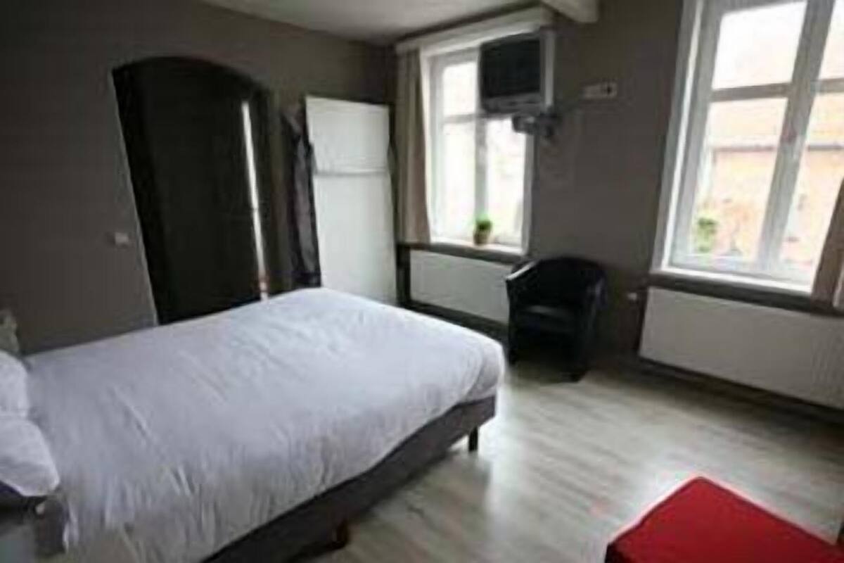 A bedroom with a bed, a chair, a TV mounted on the wall, and a window.