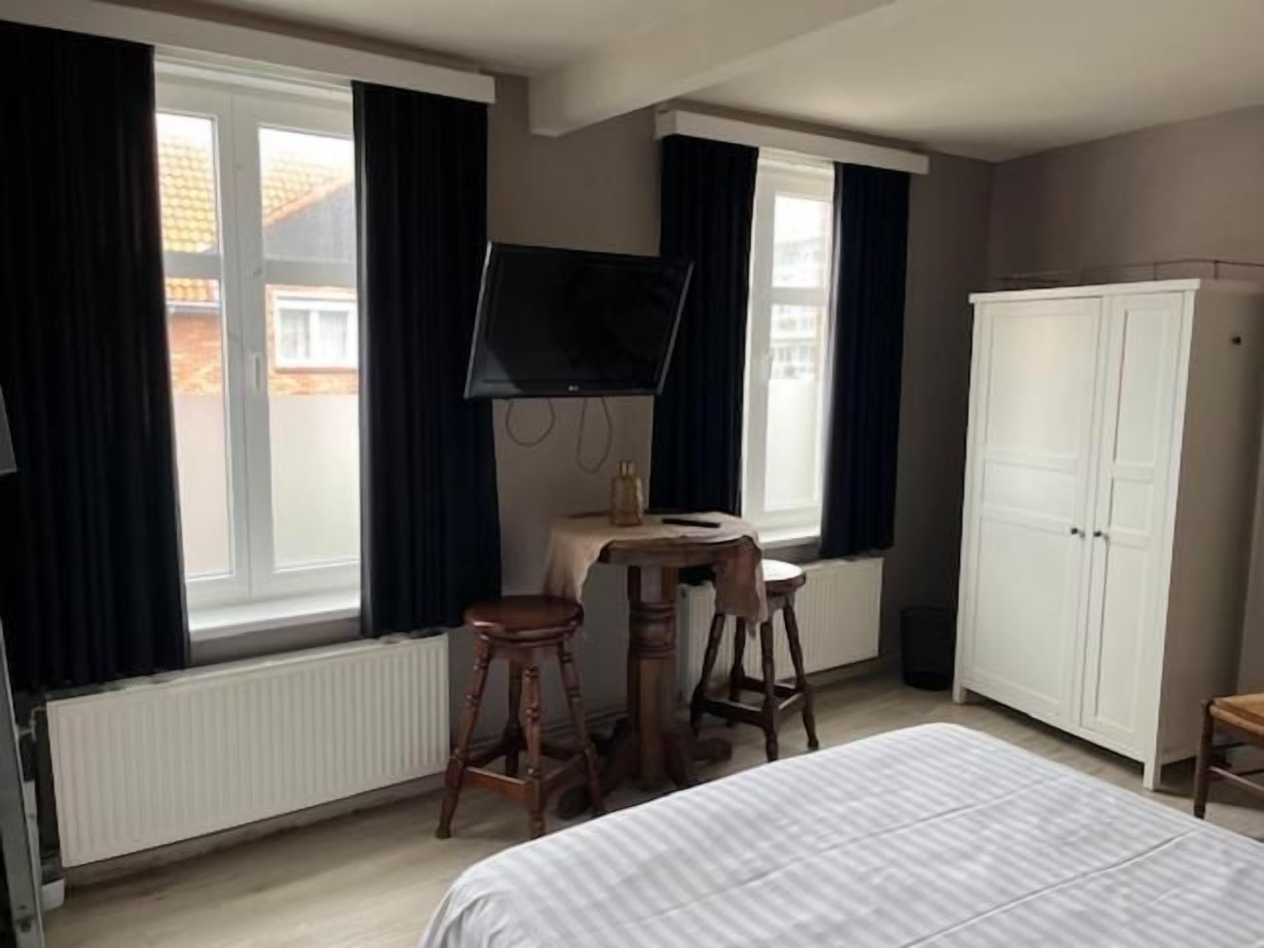 A bedroom with a bed, a desk, a chair, a wardrobe, and a television.