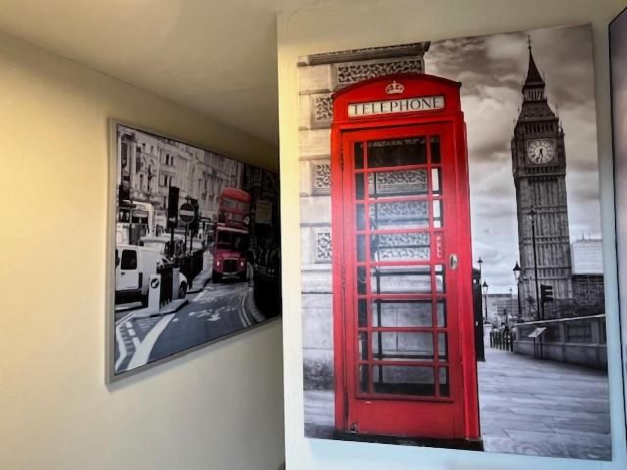 Un mur orné d’une fresque représentant une vue urbaine en noir et blanc, avec une cabine téléphonique rouge.