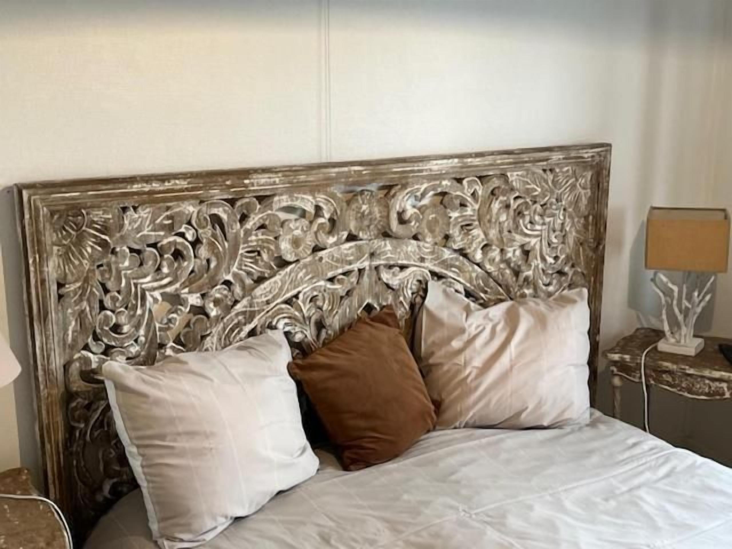A bed with a decorative headboard, two pillows, and a bedside table with a lamp.