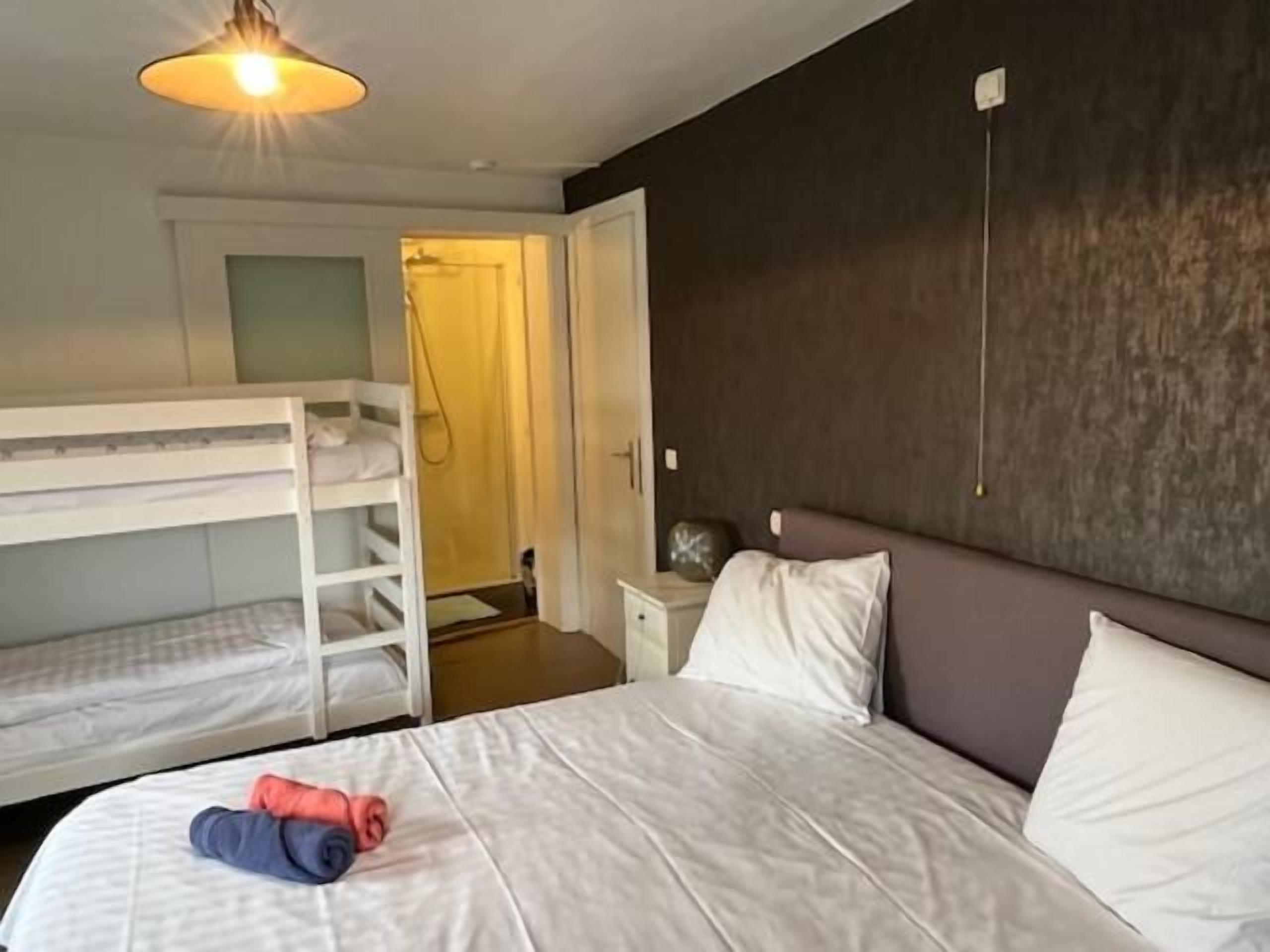 A hotel room with a bunk bed, a single bed, a nightstand, and a bedside table.