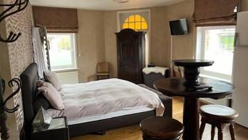 Ein Schlafzimmer mit einem Bett, einem runden Tisch mit Hocker, einem Fernseher und einem Fenster mit Vorhängen.