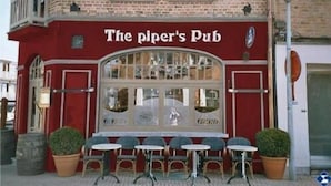 The Piper's Pub with a red facade, a large window, and outdoor seating with tables and chairs. - The Piper's Pub (Middelkerke)