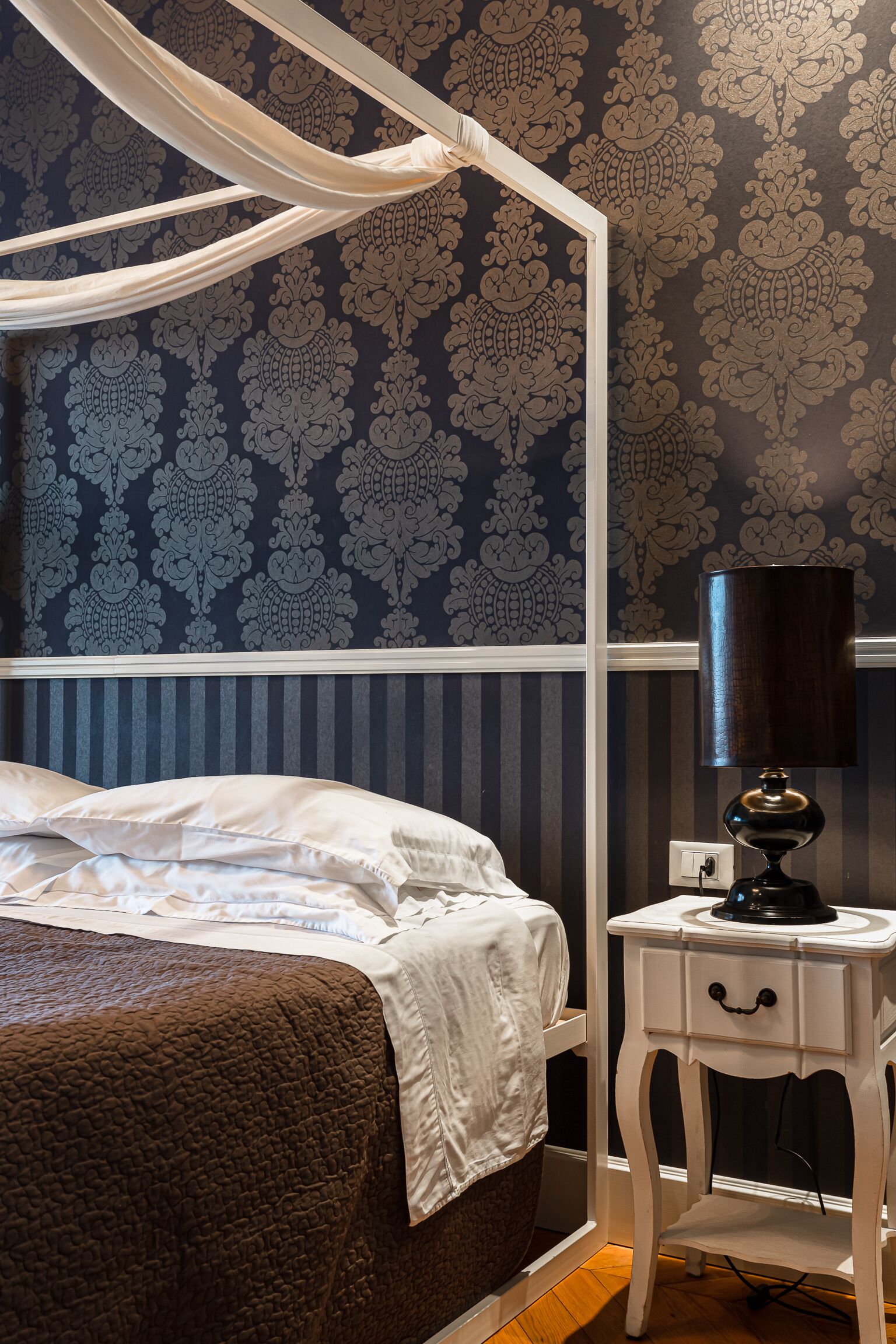 Une chambre à coucher avec un lit à baldaquin, une table de chevet avec une lampe et un papier peint à motifs.