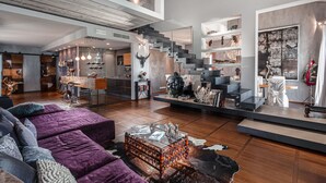 Un vaste espace de vie agrémenté d’un escalier moderne, d’un coin salon avec un canapé violet et d’une table basse en verre.