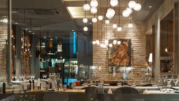 L’intérieur d’un restaurant, avec des tables dressées pour le service, des luminaires sphériques suspendus et un mur en briques orné d’une fresque.