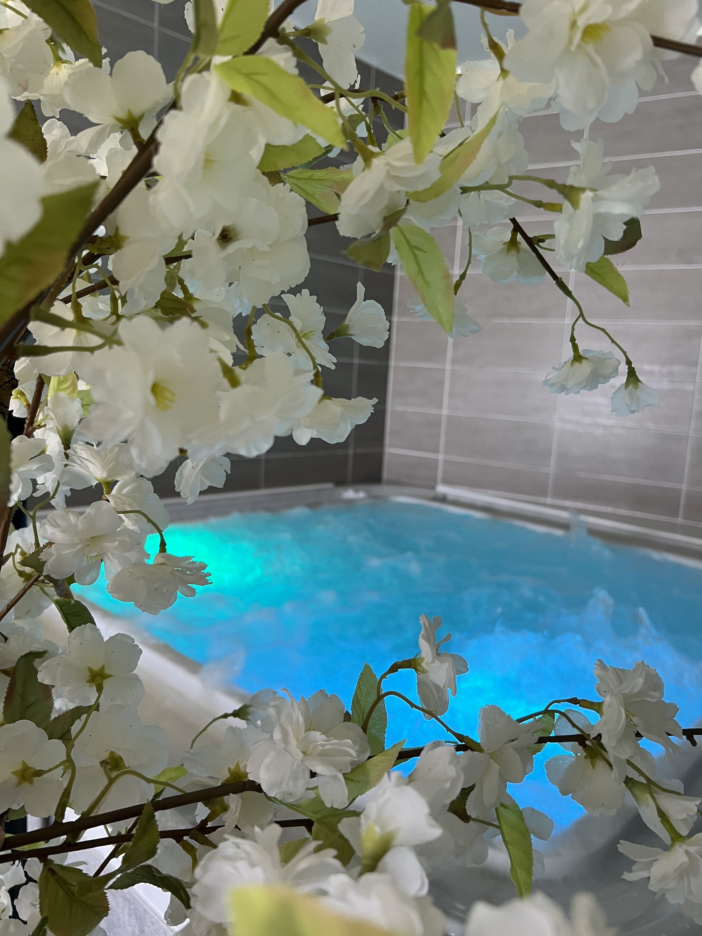 Un área de piscina con agua azul cristalina, rodeada de flores blancas y follaje verde.