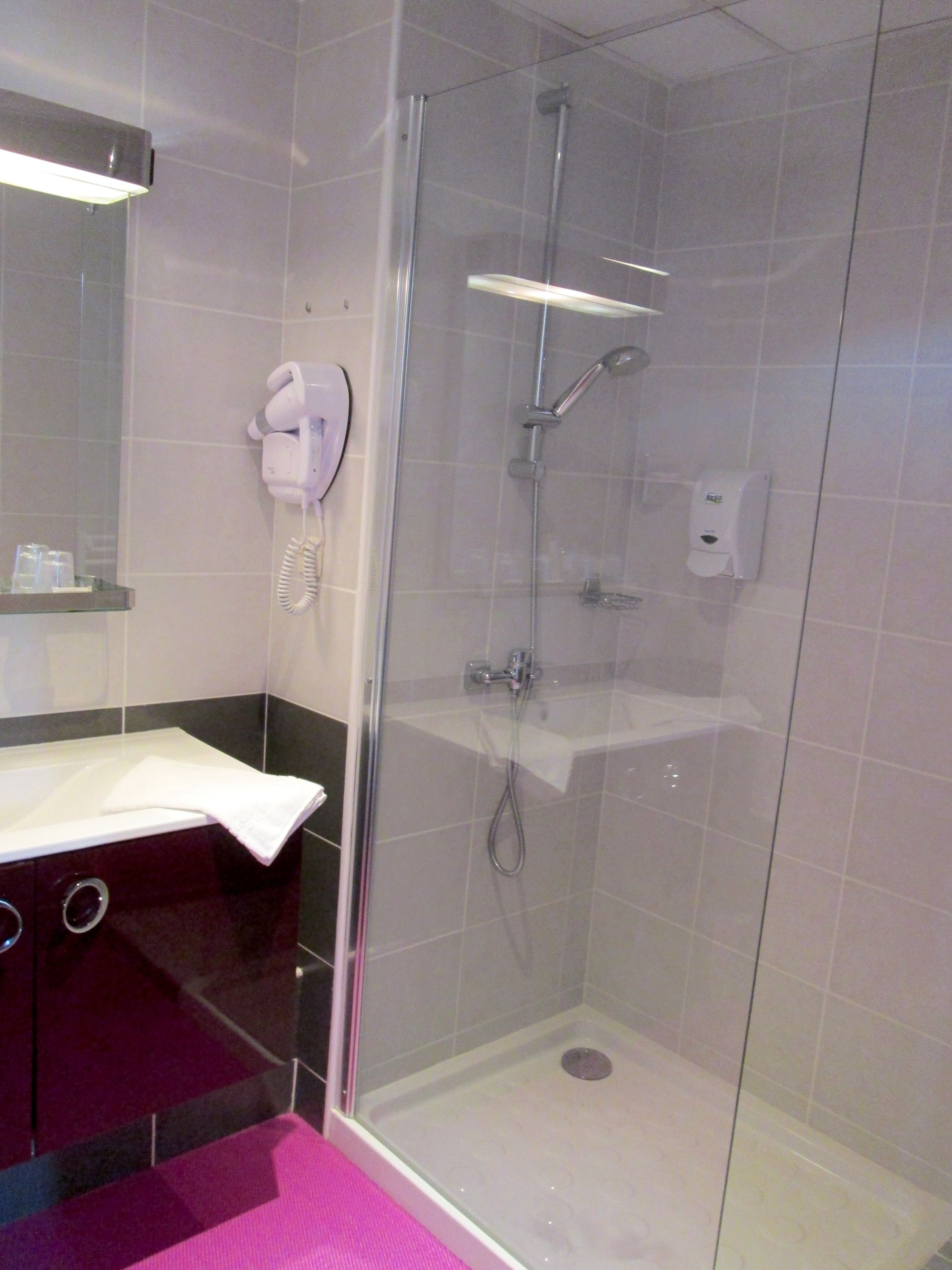 A modern bathroom with a glass-enclosed shower, a white sink, and a towel hanging on the wall.