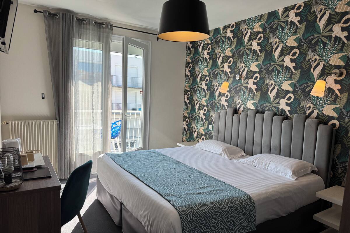 Hotellihuone, jossa on sänky, työpöytä, tuoli, patteri ja näkymä ulkopuolella olevalle parvekkeelle.