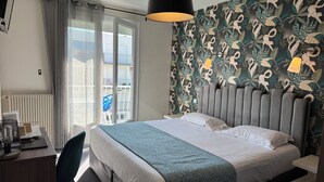 Habitación de hotel con cama, escritorio, silla, radiador y vistas al balcón exterior.