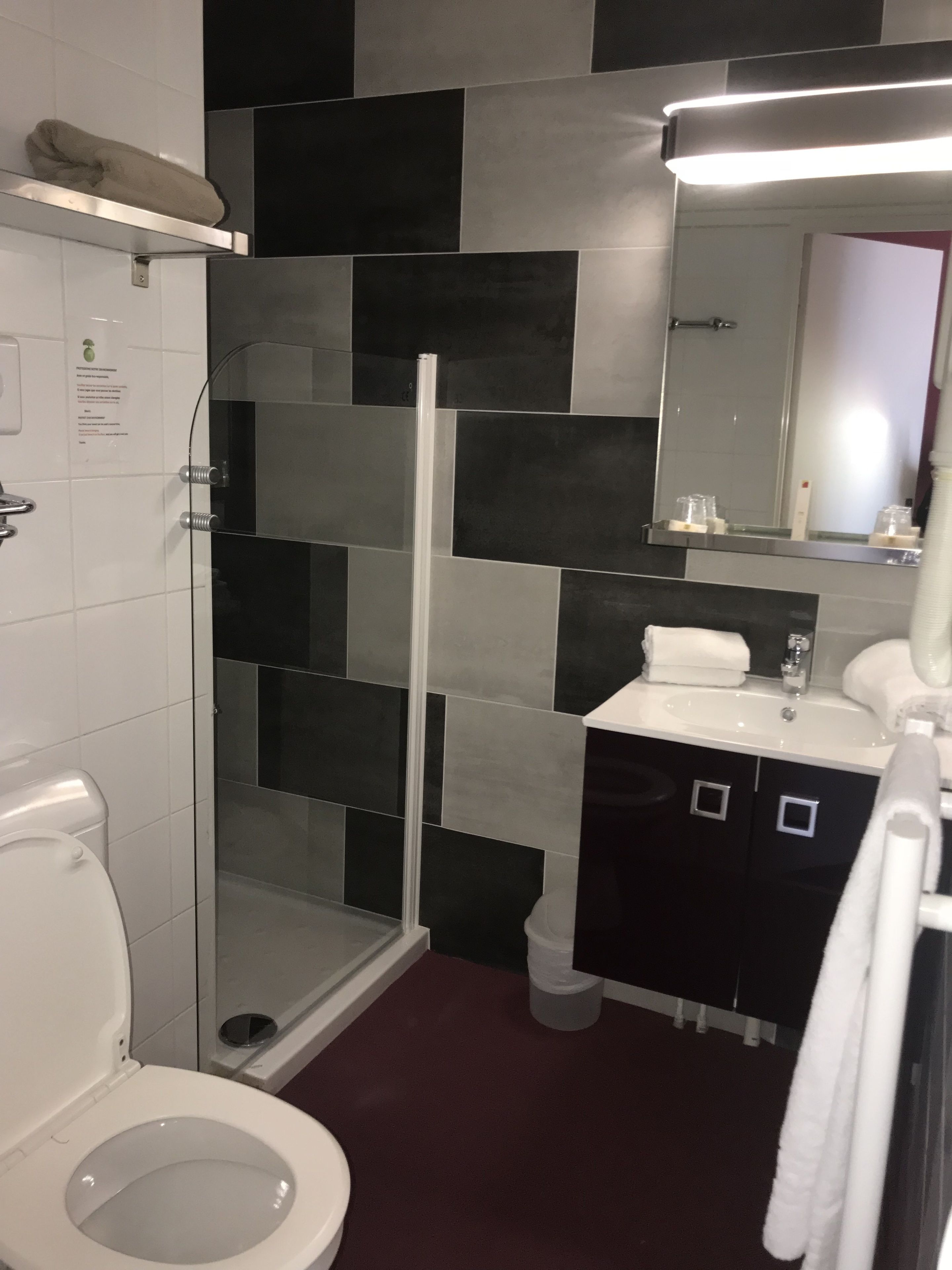 A bathroom with a toilet, a glass shower enclosure, a sink with a mirror, and a marble-tiled wall.