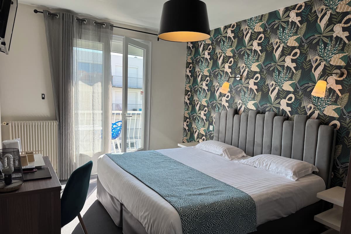 Habitación de hotel con cama, escritorio, silla, radiador y vistas al balcón exterior.