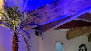 Zona de piscina con una palmera, un reloj en la pared y un muro de piedra.