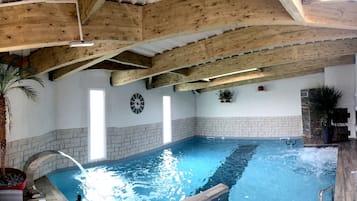 Relax by the pool surrounded by lush greenery and stone walls, with seating areas and a clock nearby.