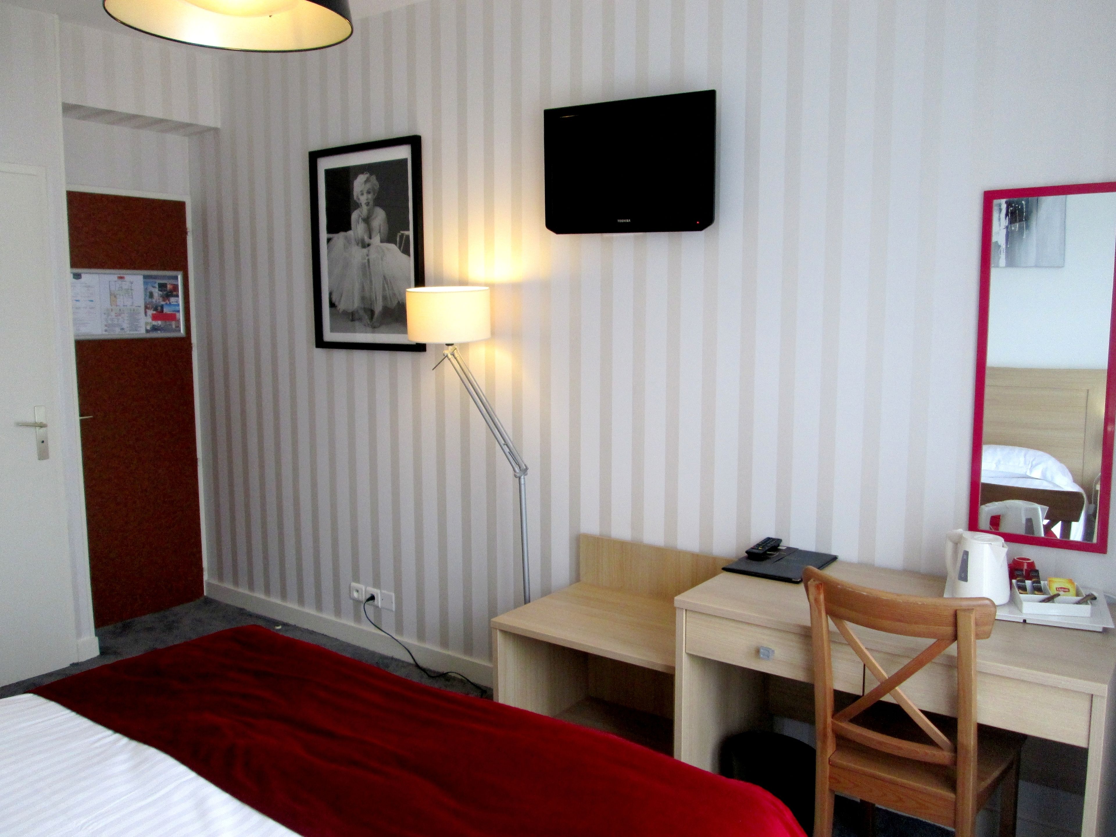 Habitació d'hotel amb llit, escriptori, cadira, televisió, làmpada i mirall.