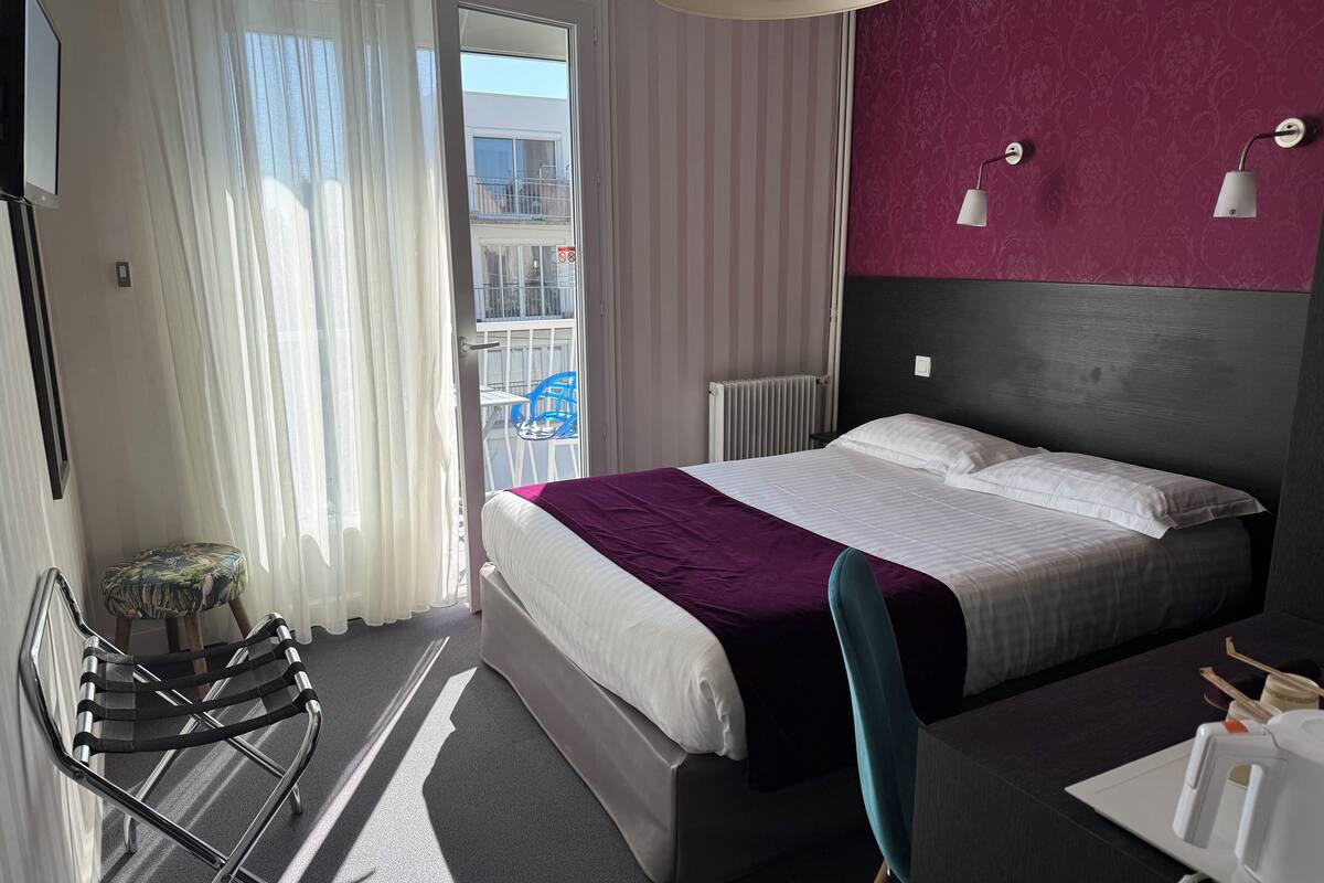 Hotellihuone, jossa on sänky, tuoli, työpöytä ja näkymä ulkopuolella olevalle parvekkeelle.