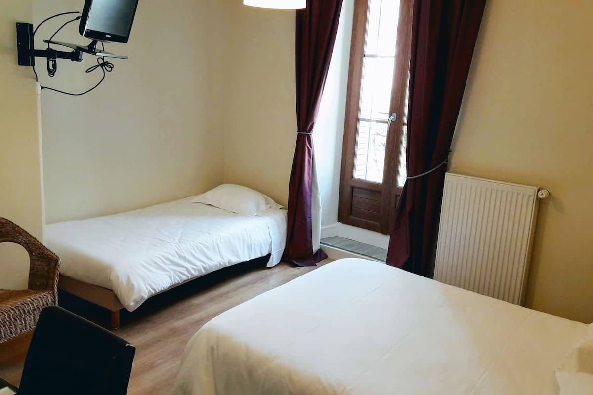 A hotel room with two single beds, a TV mounted on the wall, a wicker chair, and a radiator.