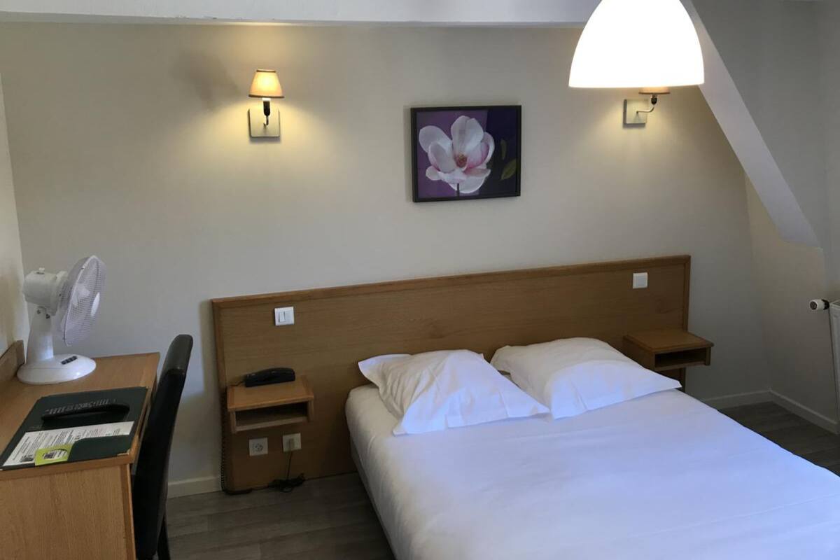 A hotel room with a bed, bedside tables, a desk with a fan, and two wall-mounted lamps.
