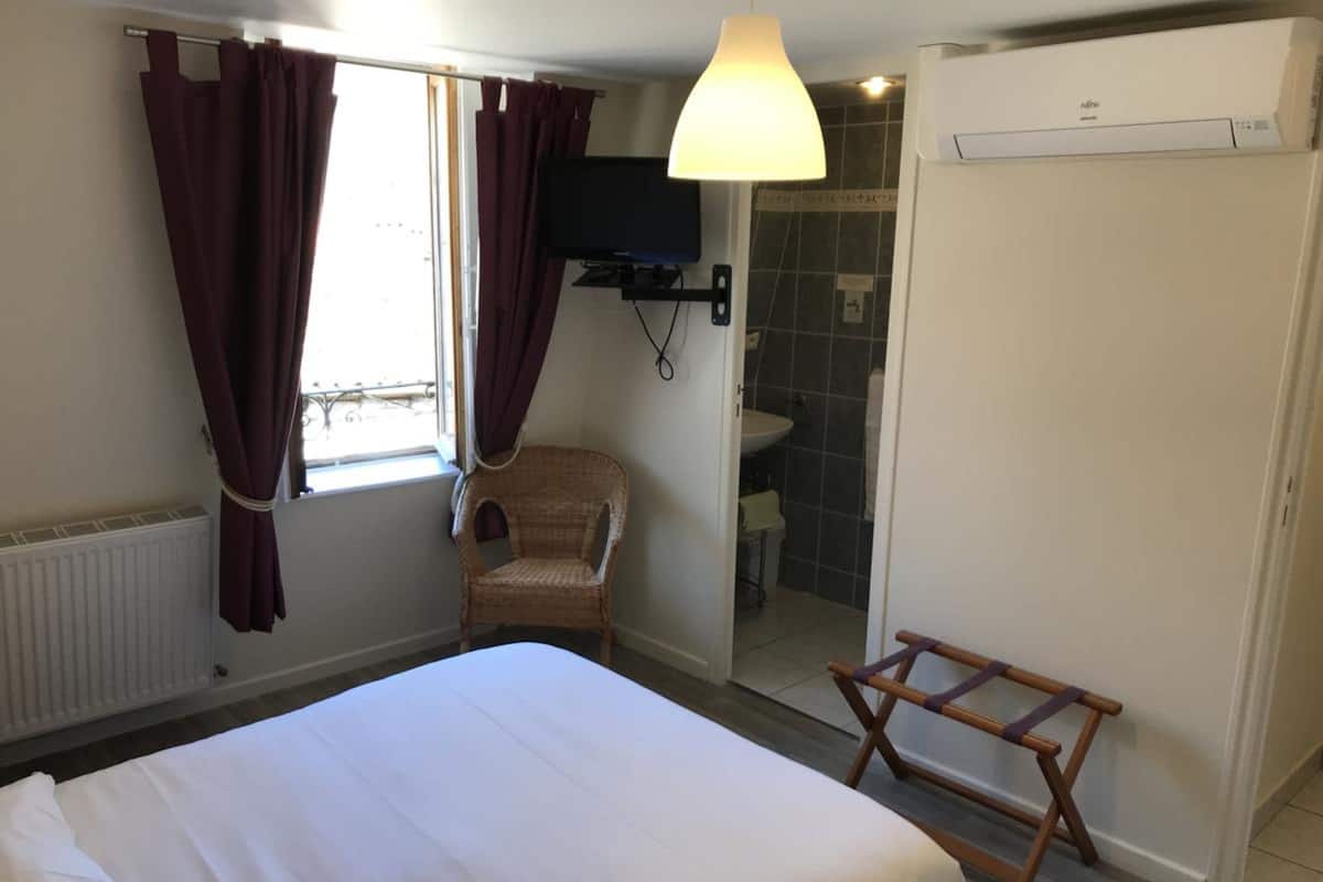 A bedroom with a bed, a chair, a TV, a shower, and a wardrobe.
