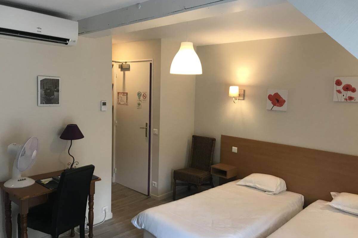 A hotel room with two beds, a desk with a chair, a lamp, and a ceiling fan.