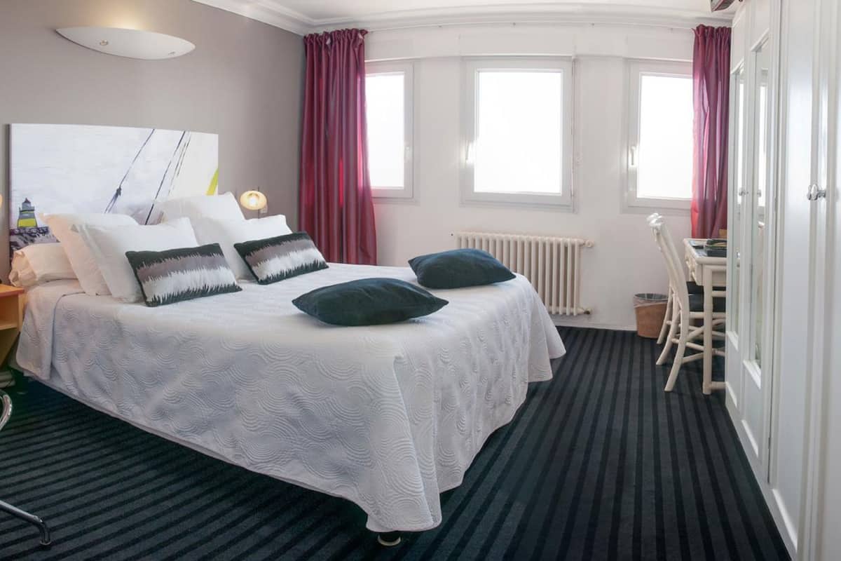 A hotel room with a large bed, two bedside tables, a desk, and a chair.